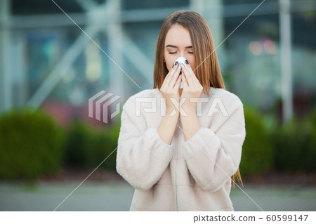 Cold and flu. Young attractive girl, caught a cold on the street, wipes her nose with a napkin 60599147