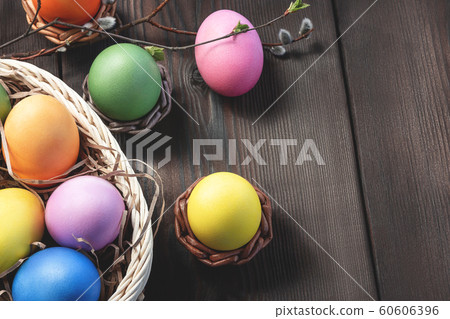 Easter composition - several colored eggs in a basket and on a dark wooden table with willow twigs, place for text, copy space 60606396