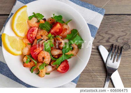Fresh homemade salad of shrimp, arugula and tomato in a white plate on a wooden table, top view, flat lay, close up 60606475