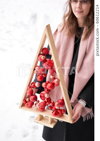 Alternative wooden christmas tree in womans hands . A handmade Christmas tree and red christmas balls. Alternative wooden christmas tree in womans hands . A handmade Christmas tree and red christmas balls. 60612214