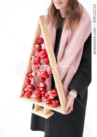 Alternative wooden christmas tree in womans hands . A handmade Christmas tree and red christmas balls. Alternative wooden christmas tree in womans hands . A handmade Christmas tree and red christmas balls. 60612218