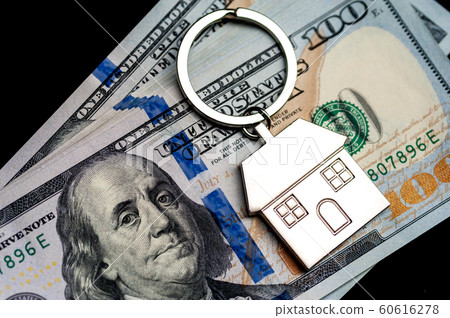 Close-up keychain in the form of house lies in it a pile of dollar bills lying on a black surface. Close-up keychain in the form of house lies in it a pile of dollar bills lying on a black surface. 60616278