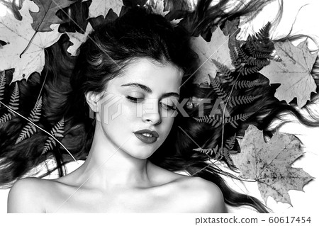 Portrait of a young brunette woman on a white background with a green fern and yellow leaves around her head Portrait of a young brunette woman on a white background with a green fern and yellow leaves around her head 60617454
