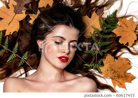 Portrait of a young brunette woman on a white background with a green fern and yellow leaves around her head 60617455