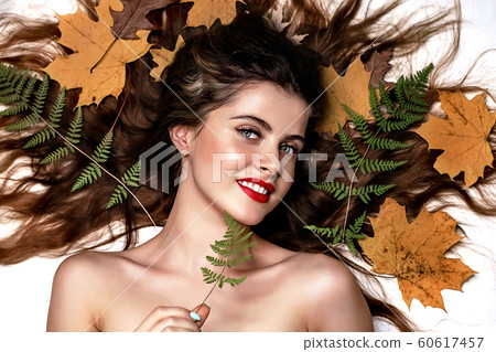 Portrait of a young brunette woman on a white background with a green fern and yellow leaves around her head Portrait of a young brunette woman on a white background with a green fern and yellow leaves around her head 60617457