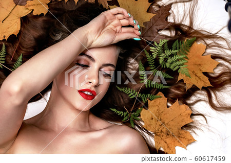 Portrait of a young brunette woman on a white background with a green fern and yellow leaves around her head Portrait of a young brunette woman on a white background with a green fern and yellow leaves around her head 60617459