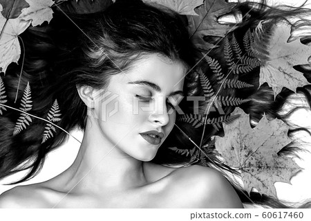 Portrait of a young brunette woman on a white background with a green fern and yellow leaves around her head Portrait of a young brunette woman on a white background with a green fern and yellow leaves around her head 60617460