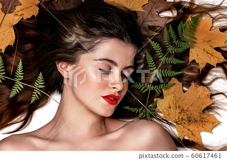 Portrait of a young brunette woman on a white background with a green fern and yellow leaves around her head Portrait of a young brunette woman on a white background with a green fern and yellow leaves around her head 60617461