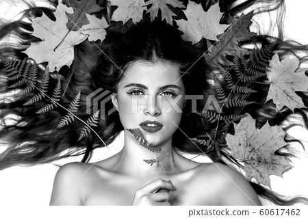 Portrait of a young brunette woman on a white background with a green fern and yellow leaves around her head Portrait of a young brunette woman on a white background with a green fern and yellow leaves around her head 60617462
