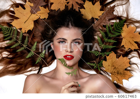 Portrait of a young brunette woman on a white background with a green fern and yellow leaves around her head Portrait of a young brunette woman on a white background with a green fern and yellow leaves around her head 60617463