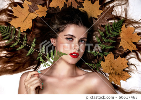 Portrait of a young brunette woman on a white background with a green fern and yellow leaves around her head 60617465