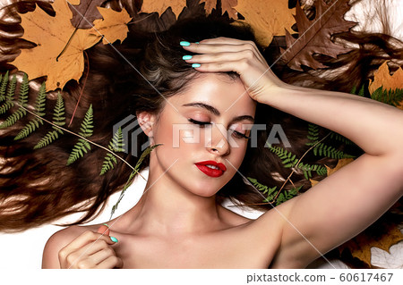 Portrait of a young brunette woman on a white background with a green fern and yellow leaves around her head Portrait of a young brunette woman on a white background with a green fern and yellow leaves around her head 60617467