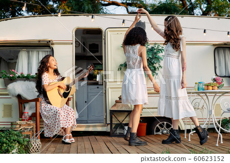 Young happy women have fun together playing guitar and dancing outdoors near their camper van Young happy women have fun together playing guitar and dancing outdoors near their camper van 60623152