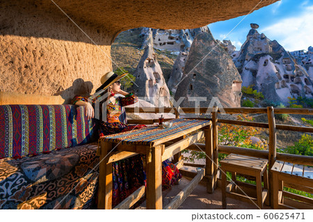 Woman in Bohemian dress sitting on traditional cave house in Cappadocia, Turkey. 60625471