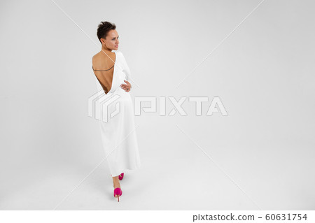 short-haired lady in elegant white dress with open back on gray background 60631754