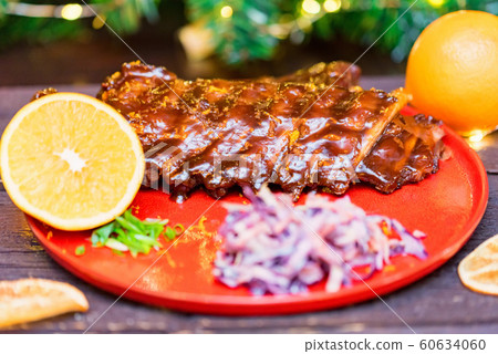Close up roasted pork ribs in orange sauce served with lemon and vegetables 60634060