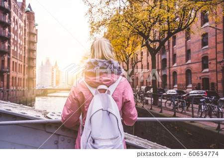 Rear view of tourist adult blond woman with backpack enjoying beautiful sunset scene on the Speicherstadt historic warehouse district in Hamburg, Germany, Europe 60634774