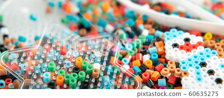 Set of perler beads. Perler pegboard, tweezers and many colorful fusible beads. Toy that develops the imagination of child. Children's toys theme. Wide background with space Set of perler beads. Perler pegboard, tweezers and many colorful fusible beads. Toy that develops the imagination of child. Children's toys theme. Wide background with space 60635275