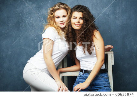 young pretty teenage girls friends with blond and brunette curly hair posing cheerful on blue background, lifestyle people concept young pretty teenage girls friends with blond and brunette curly hair posing cheerful on blue background, lifestyle people concept 60635974