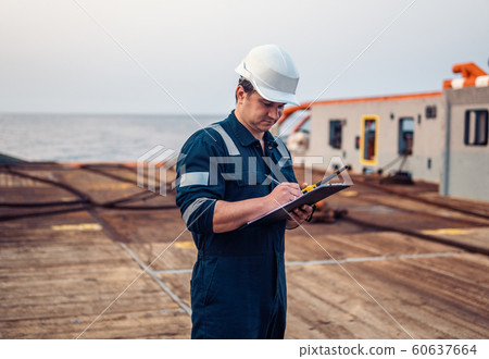 Deck Officer on deck of offshore vessel or ship , wearing PPE personal protective equipment. He fills checklist. Paperwork at sea 60637664