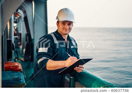 Deck Officer on deck of offshore vessel or ship , wearing PPE personal protective equipment. He fills checklist. Paperwork at sea 60637786