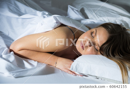 Young female in pygamas is sleeping on bed 60642155