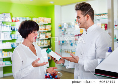Smiling man pharmacist wearing uniform assisting customers Smiling man pharmacist wearing uniform assisting customers 60642453