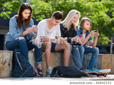 Portrait of four teenagers sitting with their mobile phones outdoors 60642553