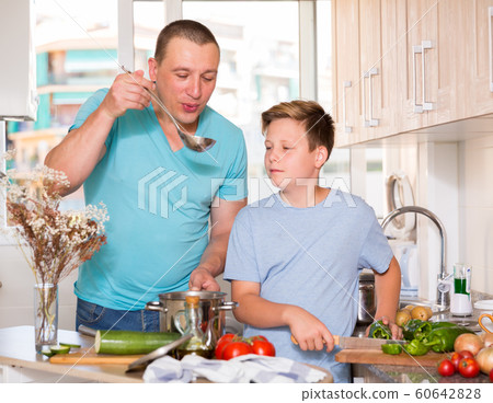 Man with his son are cooking soup in the kitchen Man with his son are cooking soup in the kitchen 60642828