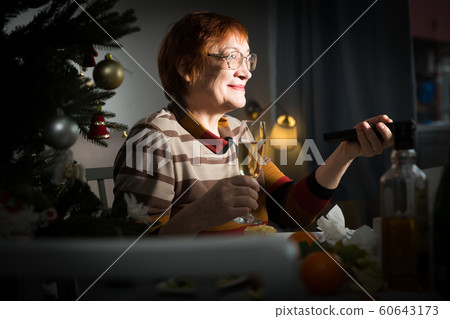 Senior woman with remote control in hand watching TV on New Year night Senior woman with remote control in hand watching TV on New Year night 60643173