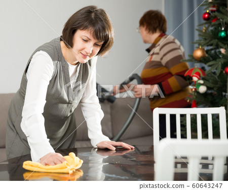 Woman wiping table, elderly mother vacuum cleaning sofa Woman wiping table, elderly mother vacuum cleaning sofa 60643247