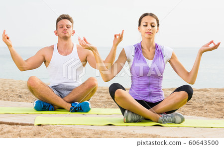 Cross-legged couple practice yoga on beach in morning Cross-legged couple practice yoga on beach in morning 60643500