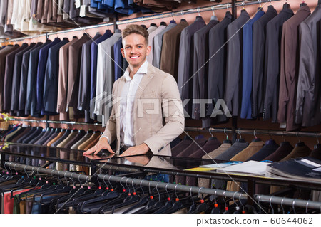Man seller displaying diverse suits in men’s cloths store Man seller displaying diverse suits in men’s cloths store 60644062
