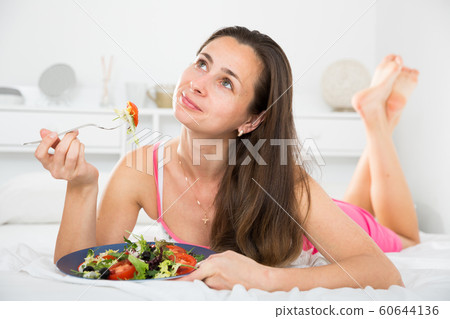 Woman eating an appetizing salad in bed Woman eating an appetizing salad in bed 60644136