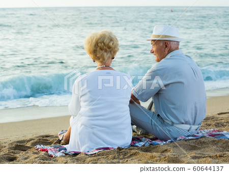 Mature man and woman sitting back on towel Mature man and woman sitting back on towel 60644137