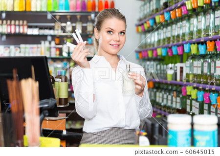 Positive salesgirl suggesting perfume in modern cosmetic store 60645015