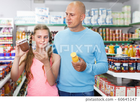 Girl with father looking different goods in supermarket Girl with father looking different goods in supermarket 60645147