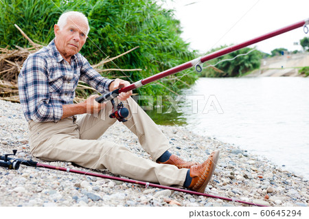 Aged man fishing at lakeside Aged man fishing at lakeside 60645294