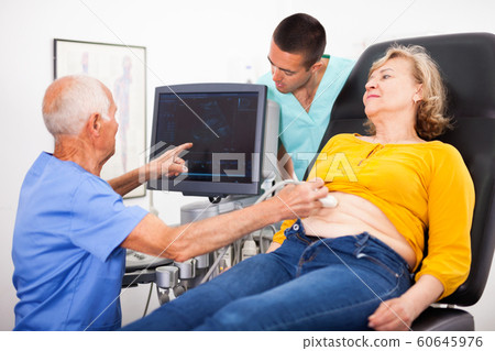 Skilled doctor with assistant diagnosing patient using ultrasonography scanner in private clinic 60645976