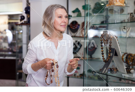 Woman trying on a gemstone necklace and earrings at a jewelry store 60646309