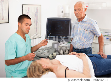 Professional sonographer explaining results of ultrasound diagnostic to female patient and her husband 60646392