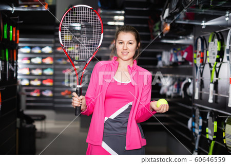 Sporty female is demonstraiting new rocket and ball for tennis in the store. Sporty female is demonstraiting new rocket and ball for tennis in the store. 60646559