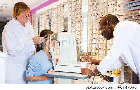 Two optometrists testing eyesight of woman 60647356