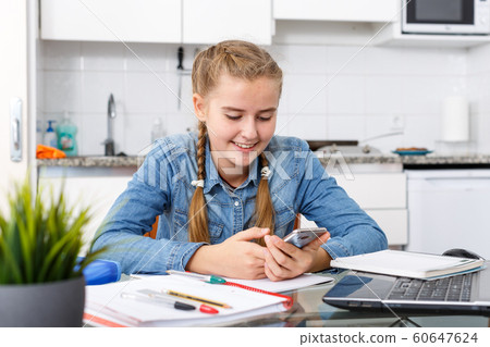 Girl doing home task using mobile phone Girl doing home task using mobile phone 60647624