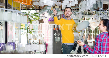 man and girl in lighter shop choosing modern round glass ceiling lamp for house man and girl in lighter shop choosing modern round glass ceiling lamp for house 60647731
