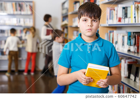 Tween boy with book in school library 60647742