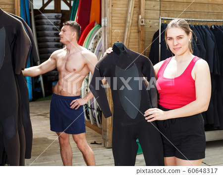 Girl choosing wetsuit in surf club Girl choosing wetsuit in surf club 60648317