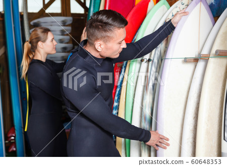 Young couple planning to surf, choosing boards and surfing suits in beach club 60648353