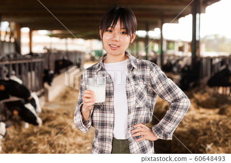 Young positive female dairy farm worker standing with glass of fresh milk Young positive female dairy farm worker standing with glass of fresh milk 60648493