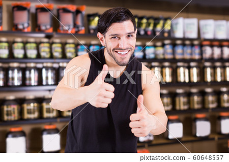 Sportman holding thumbs up in shop of sport nutrition products Sportman holding thumbs up in shop of sport nutrition products 60648557